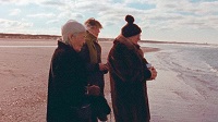 Drei Personen stehen am Strand.