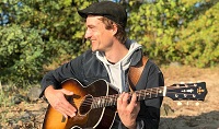 Der Musiker Phil Wood ist im Profil zu sehen, wie er lächelnd Gitarre spielt.