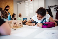 Mädchen sitzt am Tisch und schreibt.