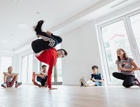 Eine Person tanzt Breakdance; andere Personen schauen dabei zu.