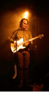 Foto zeigt den Musiker Peter Broderick im Scheinwerferlicht auf einer Bühne mit E-Gitarre.