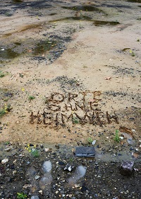 Auf einem sandigen Erdboden sind die Worte "Orte ohne Heimweh" eingeritzt.