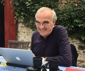 Fotografie zeigt Wilhelm Gruber am Tisch sitzend mit einem aufgeklappten Laptop vor sich.