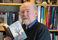 Porträtfoto von Georg Bühren, der mit seinem Buch in der Hand vor einem Bücherregal steht.