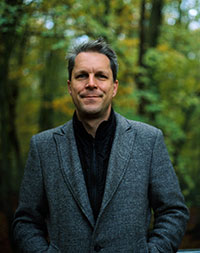 Porträtfoto von Oliver Geister, der in einem Wald steht.