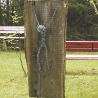 Aus Draht gewickelte, stilisierte Figur an Holzbalken