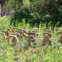 Große Holzbuchstaben, in vier Reihen, mit den Buchstaben S A T O R auf einer Wiese