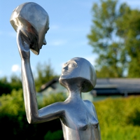 Silberne Figur betrachtet einen Kopf, den sie in ihrer Hand trägt