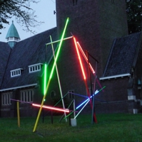 Verschiedenfarbige Neonröhren stehen gegeneinander gelehnt vor einer Kirche.