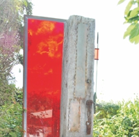 Stele aus roter Plexiglasscheibe im Metallrahmen und altem Holzpfosten