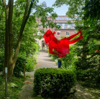 Silhouette eines schaukelnden Mädchens aus rotem Plexiglas an Ketten in einem Baum hängend