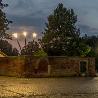 Drei Straßenlaternen lehnen an einer Mauer (Nachtansicht)