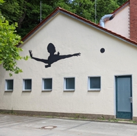 Silhouette einer Person mit Ball, an einer Hauswand