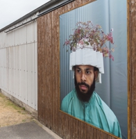 Große Portraitaufnahmen von Personen mit bepflanzter Kopfbedeckung an Scheunentoren