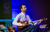 Der kurdische Musiker Dana Moheddin sitzt in blauem Theaterlicht auf einer blauen Bank und spielt auf der Tar.