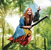 Die Schauspielerin Karoline Herfurth reitet als Hexe verkleidet auf einem Besenstil durch den Wald. Vor ihr sitzt ein schwarzer Rabe.
