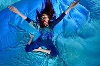 Die Tänzerin in einem blauen Kostüm sitzt mit ausgebreiteten Armen auf einem blauen Seidentuch. Das Foto ist aus der Vogelperspektive aufgenommen.