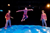 Zwei Schauspielerinnen und ein Schauspieler springen auf einem bühnenfüllenden Springkissen.
