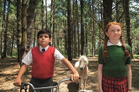 Ein schwarzhaariger Junge und ein rothariges Mädchen mit Zöpfen stehen sehr gerade in einem Wald. Zwischen ihnen befindet sich ein weißes Pony.