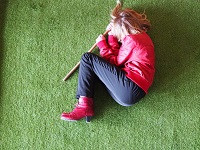 Ein Mädchen liegt eingerollt auf einem Stück künstlichem Rasen.