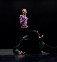 Eine Tänzerin im Vordergrund liegt am Boden und stützt ihren Kopf auf der Hand. Im Hintergrund posiert ein Tänzer stehend mit einer Hand vor der Brust.