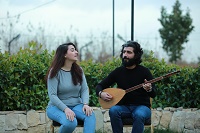 Die Sängerin Faten Ahmed und der Musiker Riyad Osman sitzen vor einem Mäuerchen im Grünen. Riyad Osman hält ein Instrument in den Händen.
