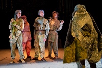 Eine Gruppe von vier Schauspielerinnen und Schauspielern stehen einer Person, in Fell gekleidet, in provokanter Haltung gegenüber.