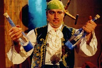 Der Schauspieler Christoph Bäumer hält verkleidet als ‚Stolperjan‘ jeweils eine Flasche in einer Hand. Er schielt.