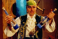 Der Schauspieler Christoph Bäumer hält verkleidet als 'Stolperjan' jeweils eine Flasche in einer Hand. Er schielt.