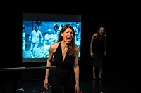 Die beiden Schauspielerinnen stehen räumlich versetzt vor einer Leinwand auf der ein Foto eines Sportwettkampfes zu sehen ist. Beide Frauen schreien.