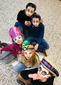 Fünf Darstellende des theaterXS, Ensemble 1 sitzen hintereinander auf dem Boden. Die Kinder tragen Masken und schauen nach oben in die Kamera.