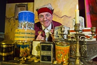 Der Schauspieler Christoph Bäumer mimt William Goldtaler. Er sitzt vor vielen hochgetürmten Dosen und hält Goldtaler in seinen Fingern.