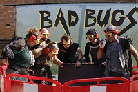 Szene aus der Vorstellung (Foto: Ursula Kaufmann) Die sechs Performenden tragen Schutzbrillen, Kopfhörer und daran befestigte Kabelbinder als Fühler. Sie schauen in eine Baugrube. Hinter ihnen steht der Schriftzug ‚Bad Bugs‘.