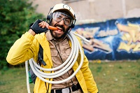 Ein Mann in gelber Jacke, mit Helm und einem Seil schräg um die Schulter gewickelt, beißt in eine Möhre.