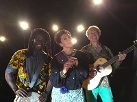 Von links nach rechts stehen Ben Diop, Josephine Kronfli und Pit Budde, die Musiker*innen vom Karibuni-Mitmachkonzert, auf der Bühne und lächeln ins Publikum.