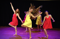 Eine Gruppe von Tänzerinnen bewegen sich seitlich durch Raum. Die Haare fliegen dabei.