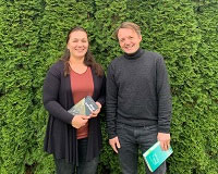 Eine Frau (Tanja Stermann, links) und ein Mann, Carsten Bender (rechts) stehen vor einer grünen Pflanzenhecke