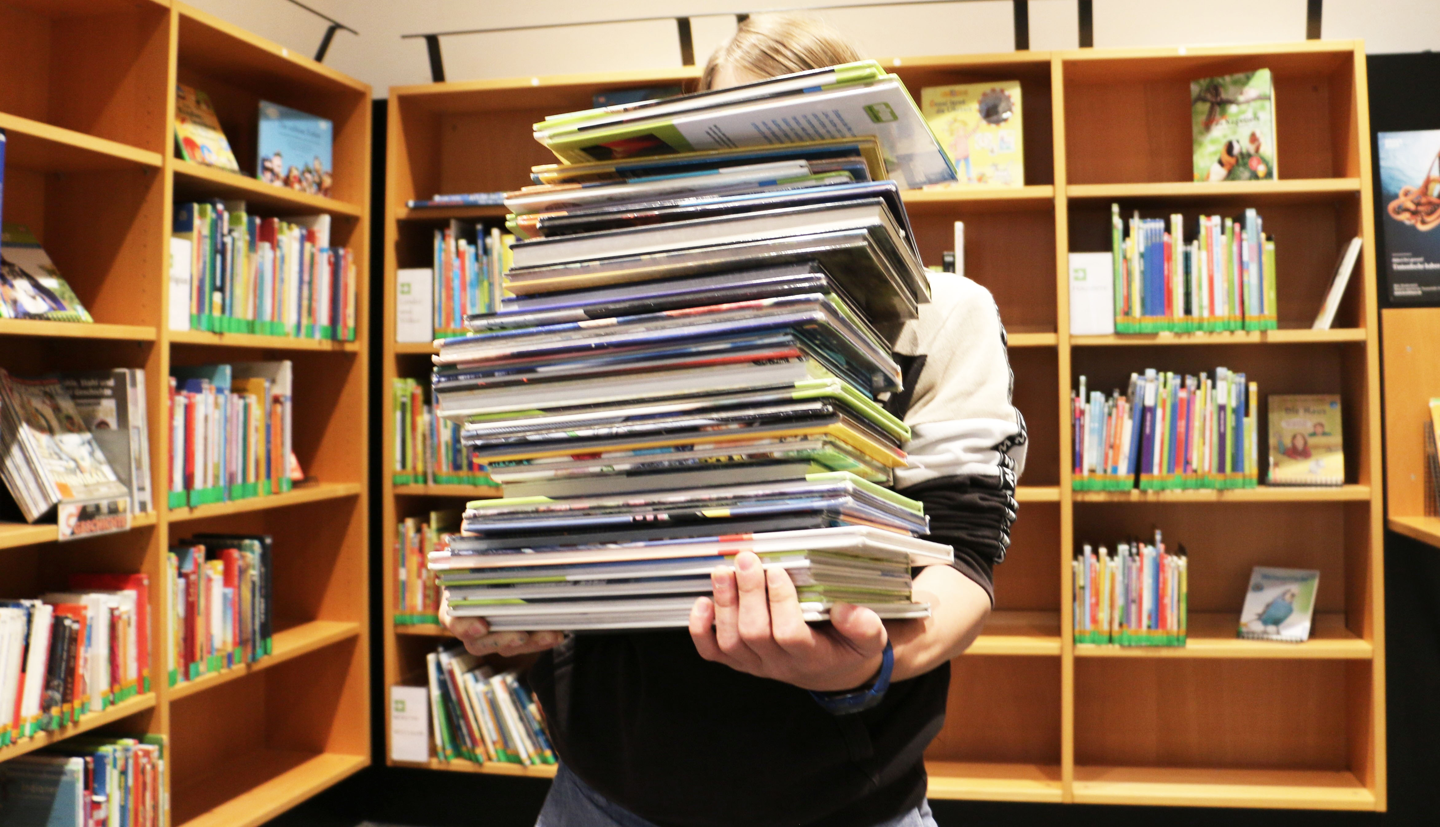 Eine Person hält einen Bücherstapel in den Armen, das Gesicht ist nicht erkennbar