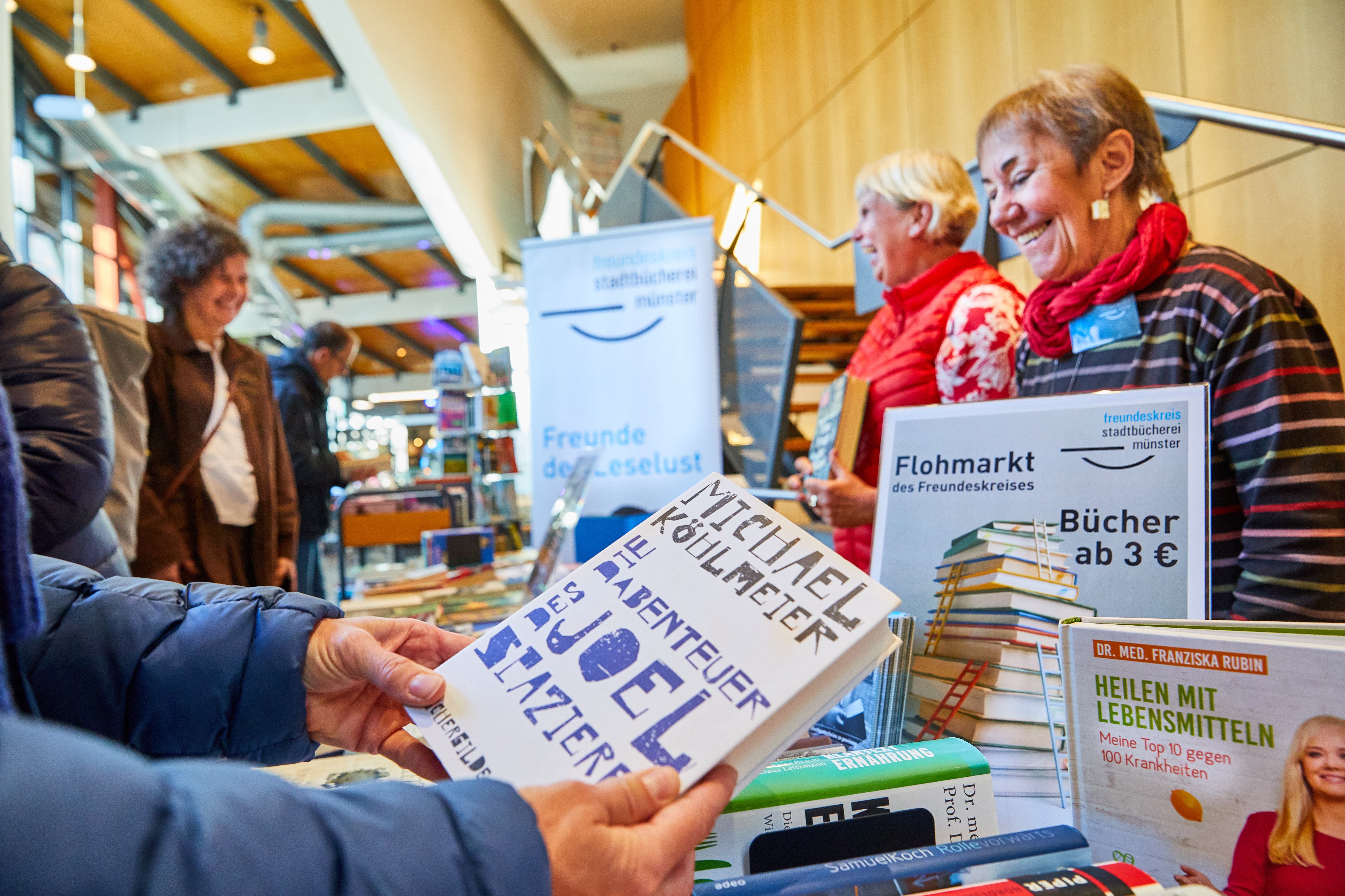 Zwei Frauen an einem Verkaufsstand im Foyer der Stadtbücherei verkaufen Bücher