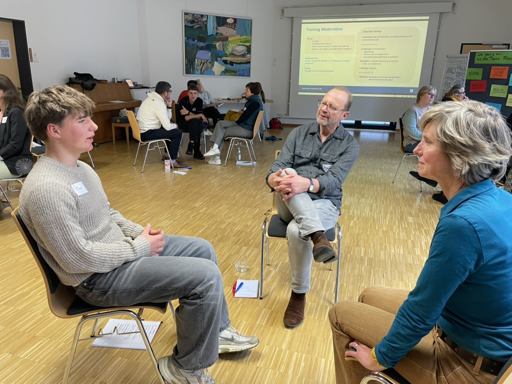 Drei Menschen sitzen sich gegenüber und unterhalten sich.