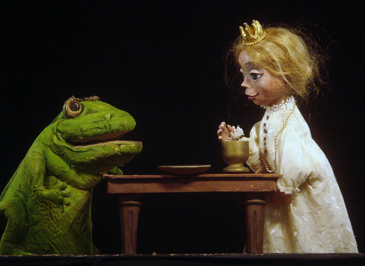 Zwei Handpuppen gegenüber an einem Tisch, ein Frosch und eine Prinzessin.