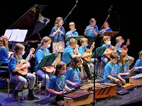 Eine Gruppe von Kindern auf einer Bühne. Sie spielen Xylophon, Gitarre, Querflöte und Klavier.