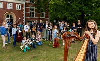 Etwa 20 Kinder stehen auf dem Rasen vor der Musikschule, jedes hat ein Instrument in der Hand - Harfe, Cello, Geige, Gitarre, , Trompete, Saxofon, Oboe, Querflöte, Blockflöte ...