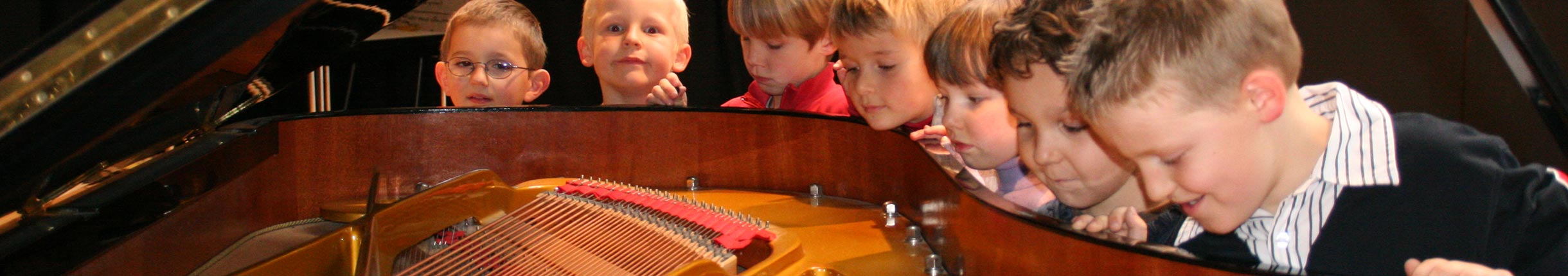 Sieben kleine Jungen schauen in ein geöffnetes Klavier.