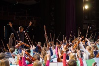 Viele Kinder mit Streichinstrumenten, vor ihnen ein Dirigent.
