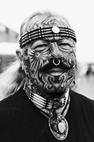 Foto eines älteren im Gesicht tätowierten langhaarigen Mannes mit Piercings.