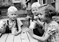 Foto von drei Kindern mit Blechtassen und Löffeln beim Essen