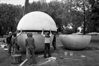 Die obere Hälfte einer übermannshohen Betonkugel wird auf eine untere Häfte hinabgelassen, sieben Männer stehen dabei oder helfen