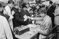 Der Entertainer Rudi Carrell sitzt hinter einem Schreibtisch und verteilt Autogramme an Menschen, die in einer Warteschlange an ihm vorbeigehen.