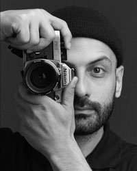 Selbstporträt des Fotografen Emad Daood. Er hält eine alte Kamera vor sein Auge, bereit ein Foto zu schießen.